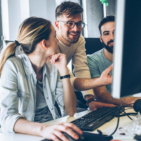 A team of 3 employees looking at a computer screen