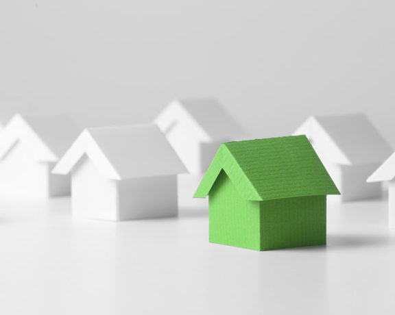 A close up of small simplified models of houses, all white with a green one in the front