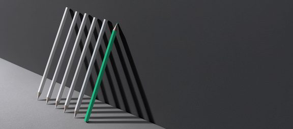 Three white and one green pencil lined up on a gray background