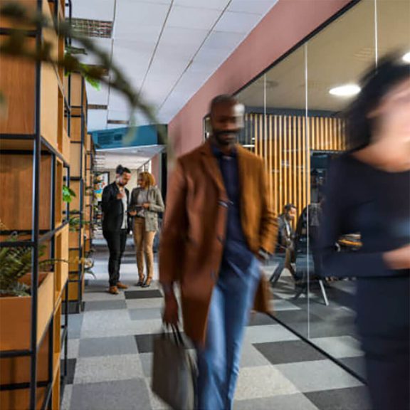 A blurred image of a person walking through an office holding a briefcase with people in the background