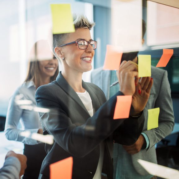 Young professionals collaborating using post it notes on a glass window